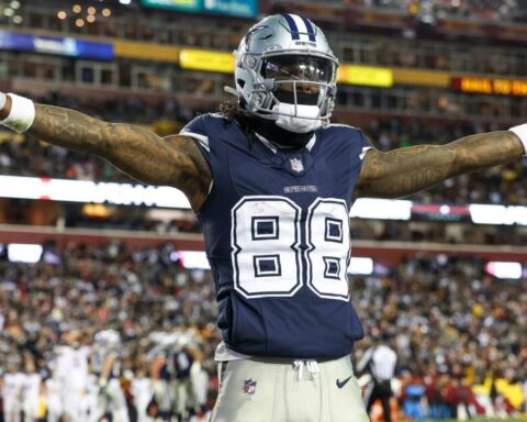 Football player wearing a Dallas Cowboys uniform with arms outstretched on the field during a game.