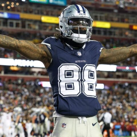 Football player wearing a Dallas Cowboys uniform with arms outstretched on the field during a game.