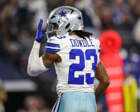 Football player in a white and blue uniform with the name "Dowdle" and number 23 on the jersey, raising his left hand.