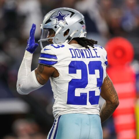 Football player in a white and blue uniform with the name "Dowdle" and number 23 on the jersey, raising his left hand.