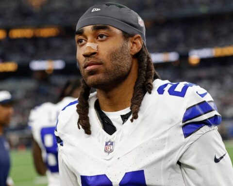 A football player in a white uniform with the number 21 stands on the field, looking ahead.