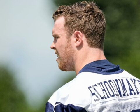 Man in a football jersey with the name "Stidham" on the back looking to the left, with a blurred green background.