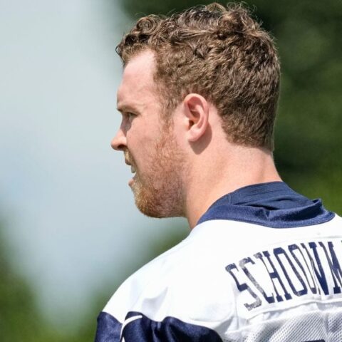 Man in a football jersey with the name "Stidham" on the back looking to the left, with a blurred green background.