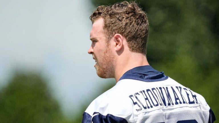 Man in a football jersey with the name "Stidham" on the back looking to the left, with a blurred green background.