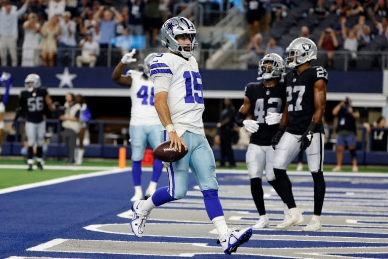Trey Lance, donning blue and white, charges down the field to score a touchdown as the players in black and white look on.
