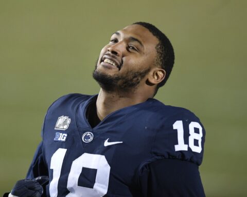 A football player in a blue jersey, number 18, looks up and smiles during a game, reminiscent of the joy seen when the Cowboys sign 2 defensive ends.