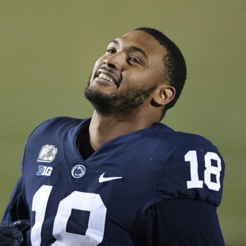 A football player in a blue jersey, number 18, looks up and smiles during a game, reminiscent of the joy seen when the Cowboys sign 2 defensive ends.