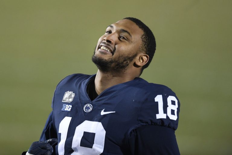 A football player in a blue jersey, number 18, looks up and smiles during a game, reminiscent of the joy seen when the Cowboys sign 2 defensive ends.