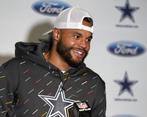 A man in a hoodie and cap stands in front of a backdrop with Ford and Dallas Cowboys logos, smiling.