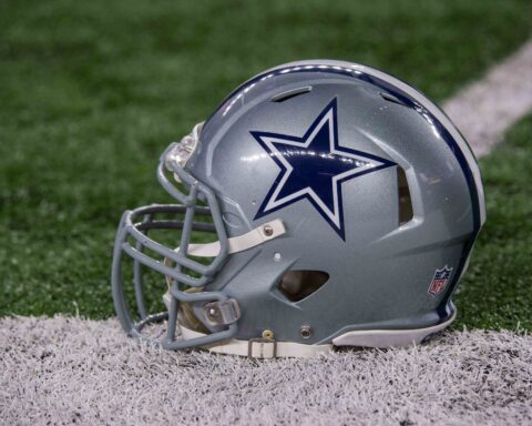 A silver football helmet with a blue star logo rests on the grass near a white line, hinting at the player who left it there.