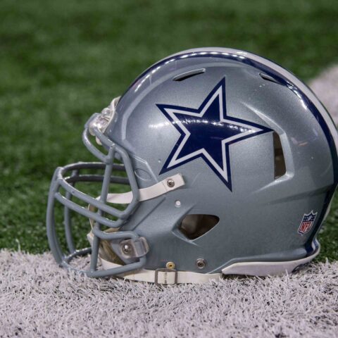 A silver football helmet with a blue star logo rests on the grass near a white line, hinting at the player who left it there.