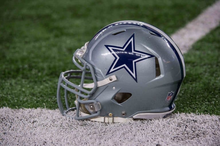 A silver football helmet with a blue star logo rests on the grass near a white line, hinting at the player who left it there.