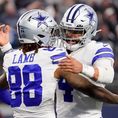 Two football players in Dallas Cowboys uniforms embrace on the field during a game.