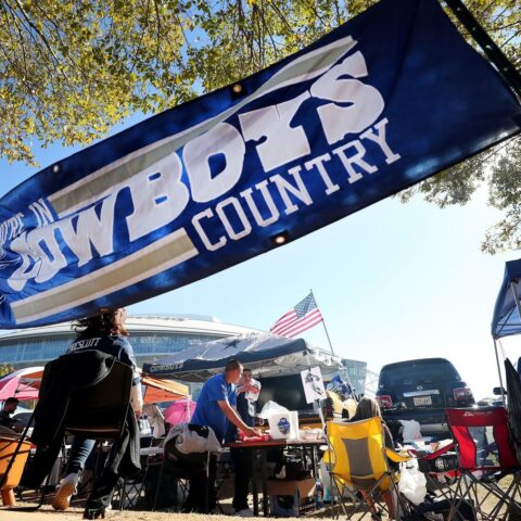 People tailgating under a "Cowboys Country" banner, with American flags and camping equipment visible in the background.