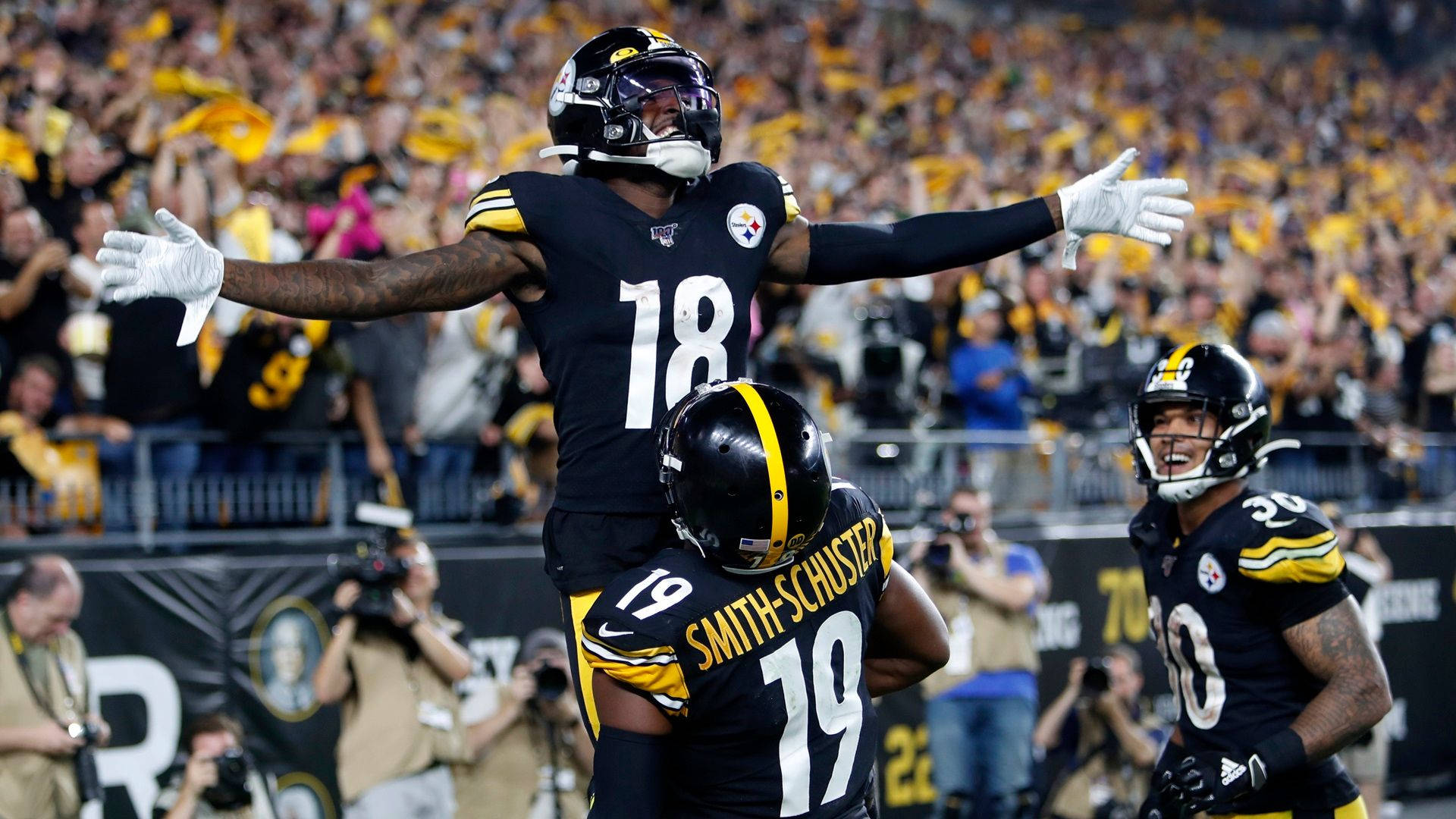 Football players in black and yellow uniforms celebrate a touchdown surrounded by a cheering crowd in a stadium.