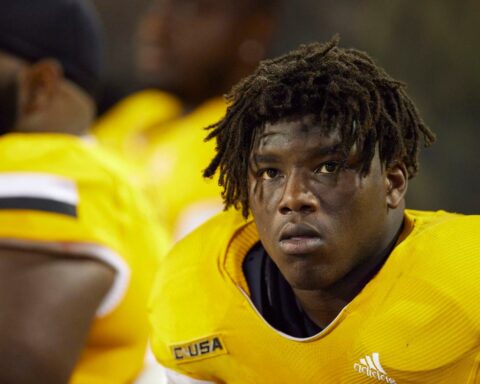 A football player wearing a yellow jersey with the text "CUSA," looking focused while on the sidelines.