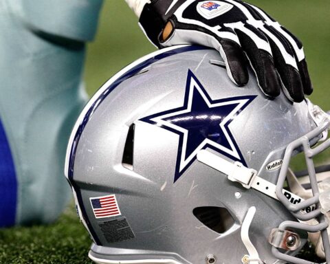 Football player resting a gloved hand on a Dallas Cowboys helmet lying on the turf.