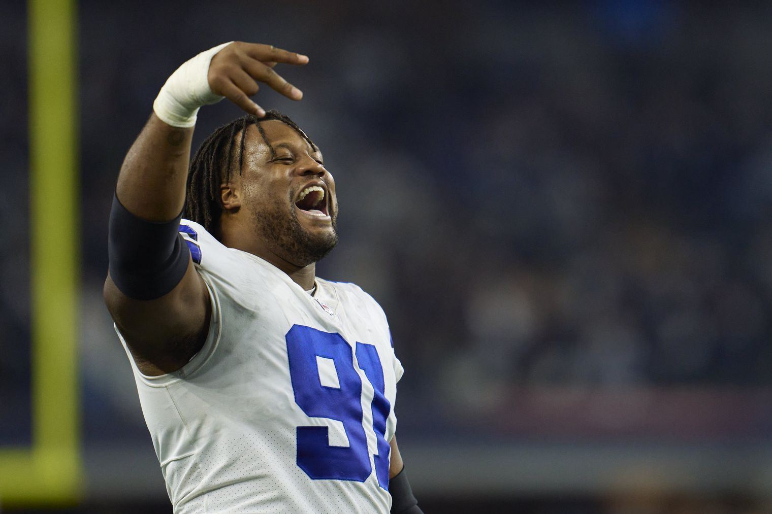 Football player in white jersey with number 91 cheers with hand gesture during a game on the field.