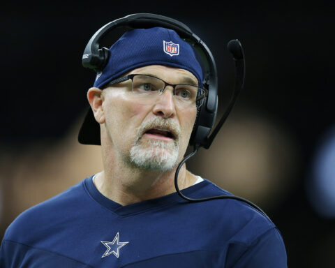 Coach in a blue NFL team shirt and a headset looks on during a game.
