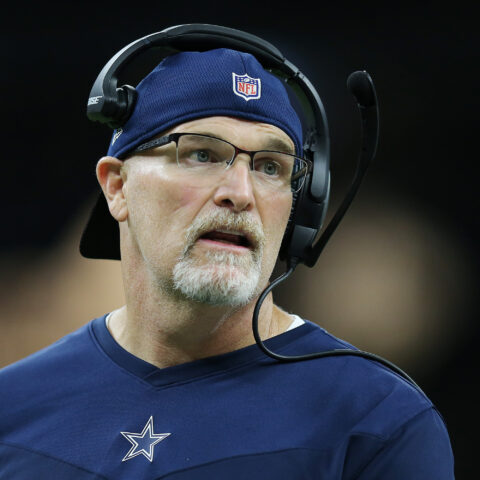 Coach in a blue NFL team shirt and a headset looks on during a game.