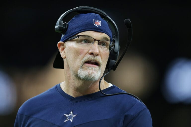 Coach in a blue NFL team shirt and a headset looks on during a game.