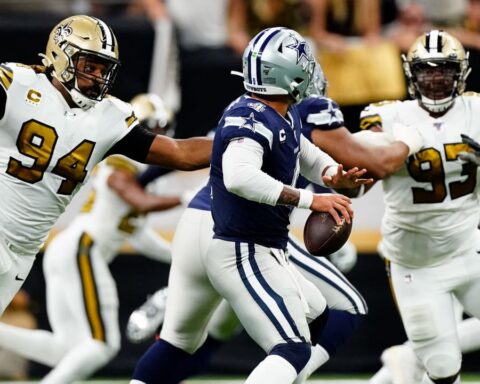 Football player in blue jersey evades two players in white jerseys on field during a game.