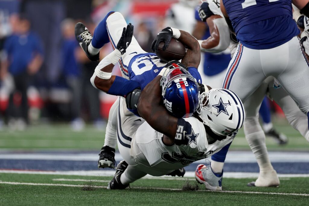 A football player in white tackles another player in blue, bringing him to the ground during a football game.