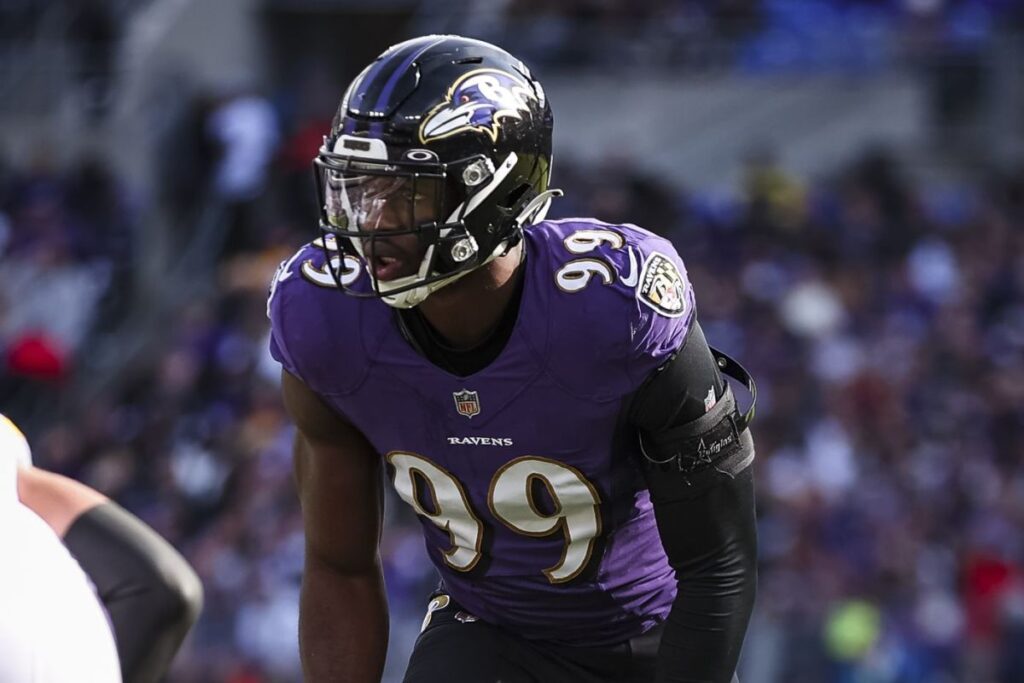 A football player wearing a purple jersey with the number 99 and a Ravens helmet on the field during a game.