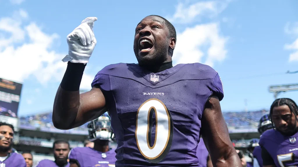 Football player in a purple Ravens jersey passionately gestures with his right hand, surrounded by teammates on the field.