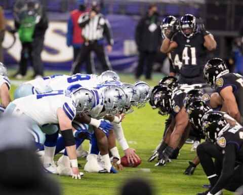 NFL teams line up for a snap, with the Cowboys in white uniforms and the Ravens in black uniforms, on a football field.