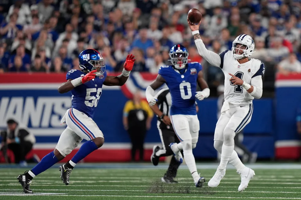 Football player throwing a pass while being pursued by a defender in a stadium filled with spectators.