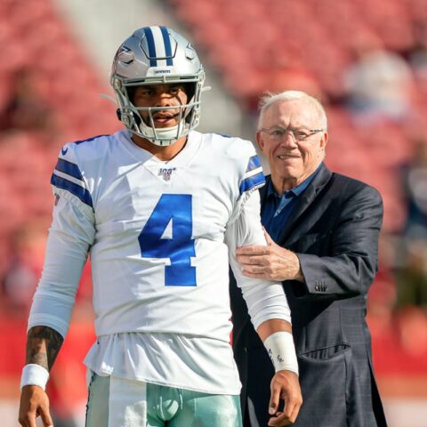 A man wearing a Dallas Cowboys football uniform stands next to an older man in a suit on a football field.