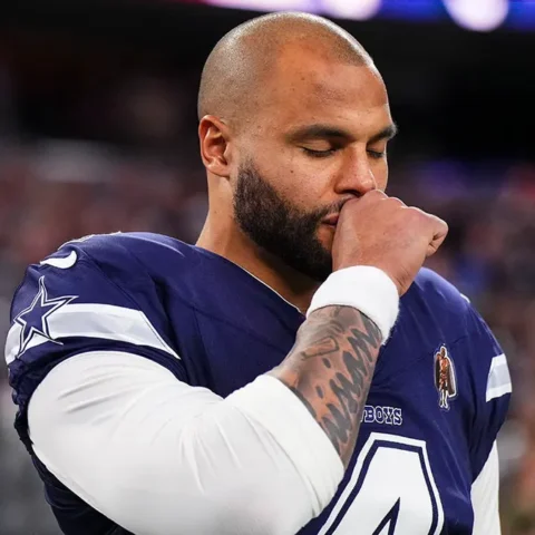 Football player in a navy jersey stands with eyes closed and hand to face on a field during a game.
