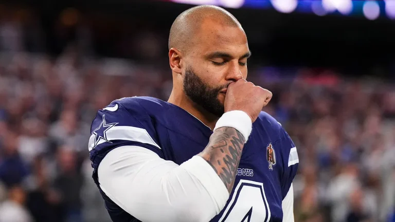 Football player in a navy jersey stands with eyes closed and hand to face on a field during a game.