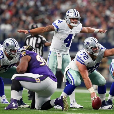 Football players from the Cowboys and Ravens are positioned pre-snap on the field during a game.