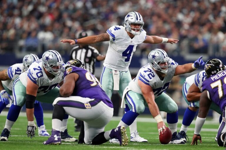 Football players from the Cowboys and Ravens are positioned pre-snap on the field during a game.