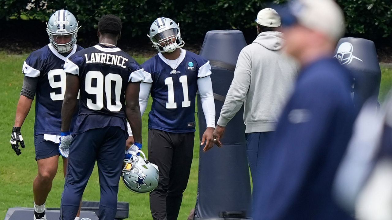 Football players in Dallas Cowboys jerseys practice on a field, with tackling dummies in the background.