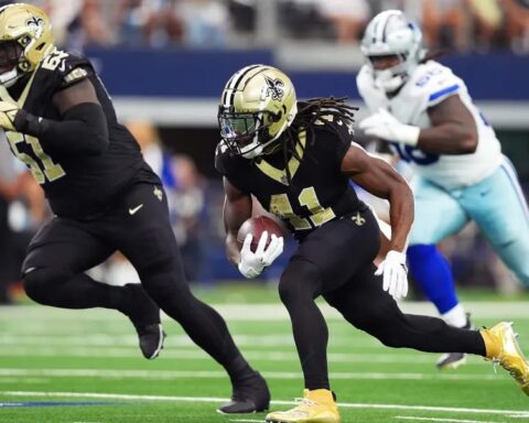 Football players from two teams in action on the field, one holding a football and running with teammates nearby.