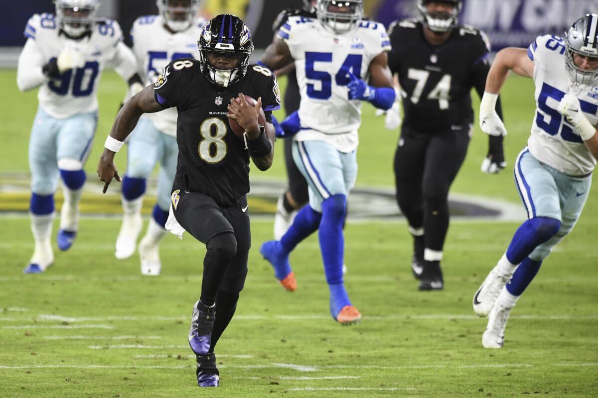 A football player in a black uniform runs with the ball while players in white uniforms chase him on the field.