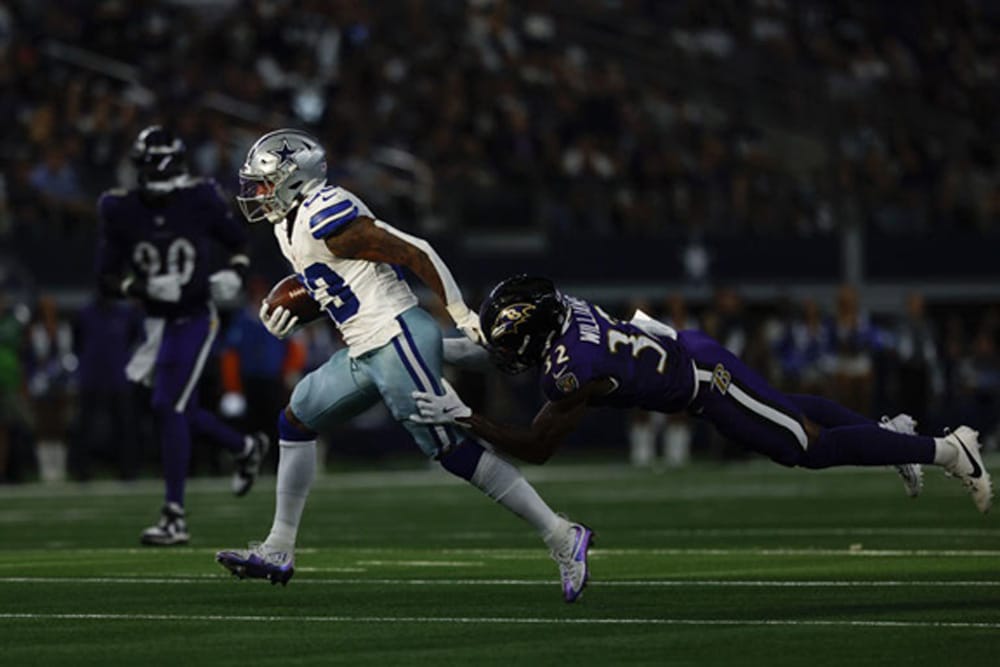 A football player in a white uniform is tackled by a player in a purple uniform during a game.