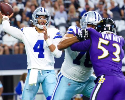 A quarterback prepares to throw the football while teammates block defensive players during a game.