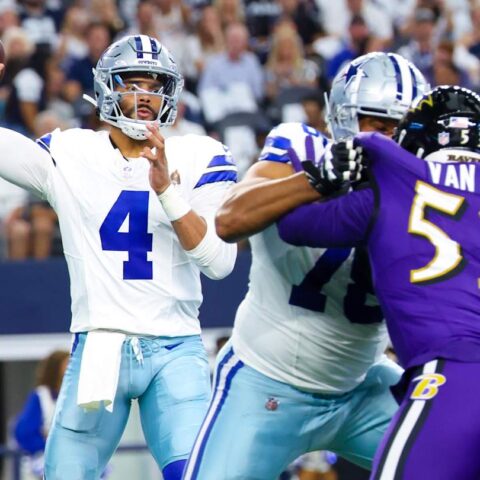 A quarterback prepares to throw the football while teammates block defensive players during a game.