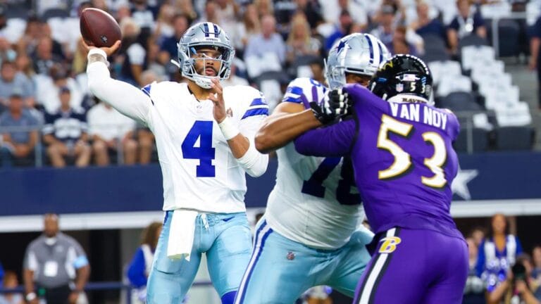 A quarterback prepares to throw the football while teammates block defensive players during a game.