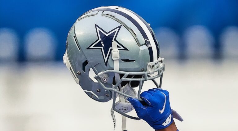 A hand in a blue glove, reminiscent of a determined player, holds up a Dallas Cowboys football helmet.