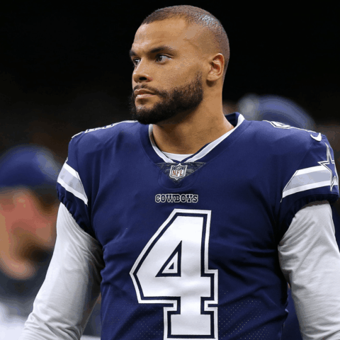 A football player in a blue Cowboys jersey with number 4 stands on the field.