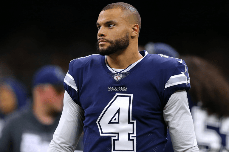 A football player in a blue Cowboys jersey with number 4 stands on the field.