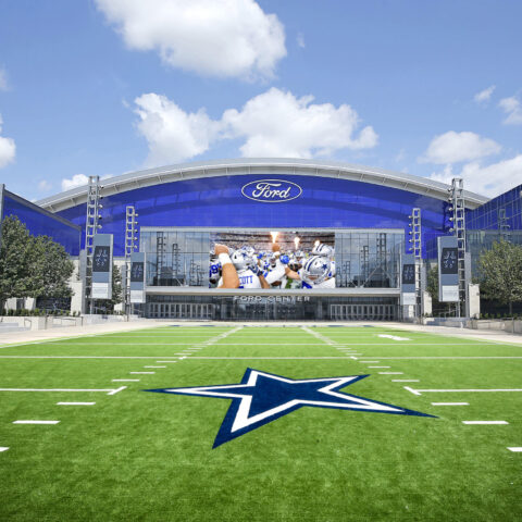 Front view of the Ford Center with the iconic Dallas Cowboys star logo on the green field, basking under a clear blue sky during Week 7.