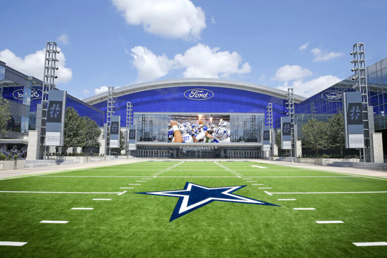 Front view of the Ford Center with the iconic Dallas Cowboys star logo on the green field, basking under a clear blue sky during Week 7.