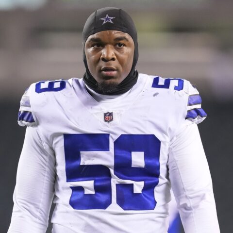 Football player wearing a Dallas Cowboys jersey and headgear, standing on a field.
