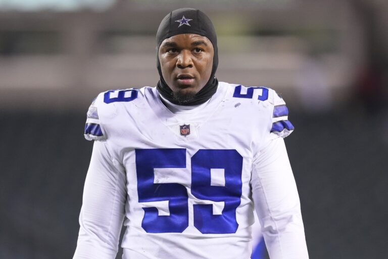 Football player wearing a Dallas Cowboys jersey and headgear, standing on a field.